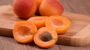 Abricots entiers et coupés en deux sur une planche de bois en gros plan