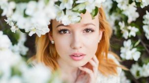 Jeune femme très jolie suite à des injections d'acide hyaluronique. Elle a les cheveux roux et regarde à travers les branchages d'un arbre en fleur.