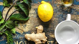 Anti-vomitifs naturels : il y a un morceau de gingembre, un citron entier, une branche de menthe verte, une tasse et de l'huile essentielle sur une vieille table en bois aux reflets bleus.