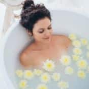 Une femme brune prend un bain. L'eau est trouble et à la surface flotte des fleurs jaunes.