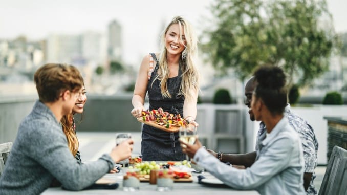 Barbecue végétal entre amis. Une fille sert des brochettes à ses quatre amis assis à table, sur un toit-terrasse.