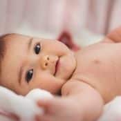 Vitamine B9 et grossesse : un petit bébé qui sourit en regardant l'objectif. Il est couché sans vêtement sur une couverture blanche.
