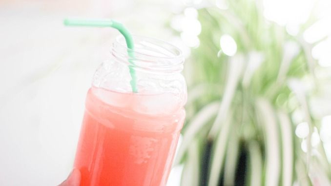 Boisson rose dans un bocal en verre avec une paille en gros plan. Plante verte en arrière plan flou