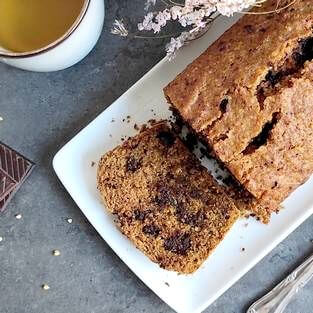 Cake au chocolat vu d'au dessus. On aperçoit une tranche de cake, une tasse de thé, des fleurs roses et un carré de chocolat sur une table grise