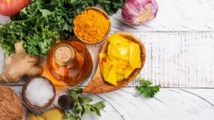 Alimentation anti candidose : on aperçoit du curcuma, du vinaire de cidre, du chou frisé, du gingembre, du kimchi et de l'ail posés sur une table en bois blanc