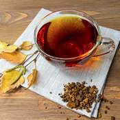 Thé de chaga (champignon) dans une tasse en verre posée sur une table en bois. Il y a des morceaux de chaga à côté et des feuilles de bouleau.