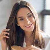 Jeune femme qui brosse ses cheveux châtains, le sourire aux lèvres, habillée de blanc.