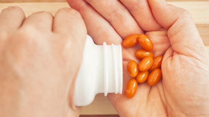 Coenzyme Q10 : une personne verse des gélules de coenzyme Q10 dans sa main. Les gélules sont oranges.