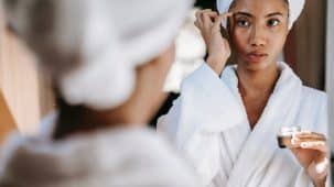 Une femme s'applique du collagène sur le visage. Elle est en peignoir et se regarde dans un miroir.