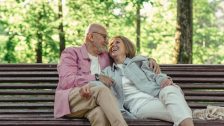 Couple de seniors heureux assis sur un banc dans la nature. L'homme et la femme s'enlacent en se souriant.