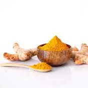 Racine (rhizome) de curcuma orange sur fond blanc. Il y du curcuma en poudre dans un bol et une cuillère à côté de la racine coupée.