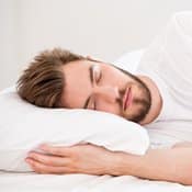 Vitamine B1 et sommeil : un jeune homme avec une barbe dormant dans un lit blanc