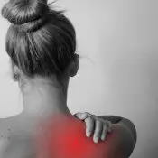 Glutathion et inflammation : une femme de dos qui se tient l'épaule avec la main. La zone est en rouge pour indiquer une douleur, une inflammation de l'articulation.