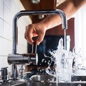 Eau filtrée qui sort d'un robinet. Un homme se sert de l'eau dans un verre.