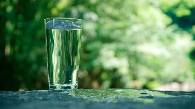 Eau pure dans un verre dans la nature. L'eau coule sur le sol.