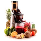 Extracteur de jus vertical sur fond blanc, entouré de nombreux fruits et légumes : ananas, pommes, cornichons, orange, gingembre, betterave, tomates, céleri, brocoli. L'extracteur sépare le jus de la pulpe et remplit deux récipients différents.