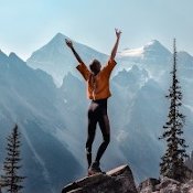 Acide alpha-lipoïque et sport : une femme heureuse debout sur un rocher, les bras levés face à la nature montagneuse et au ciel dégagé.