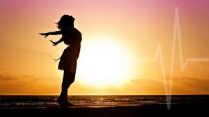 Femme qui inspire profondément les bras grand ouverts sur la plage avec le soleil et la mer en arrière plan. Rythme cardiaque discret qui se fond avec le décor.