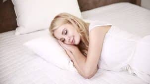 Femme blonde qui dort dans un lit blanc. Petite sourire aux lèvres.
