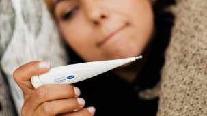 Une femme avec de la fièvre : elle est couchée et regarde son thermomètre en main