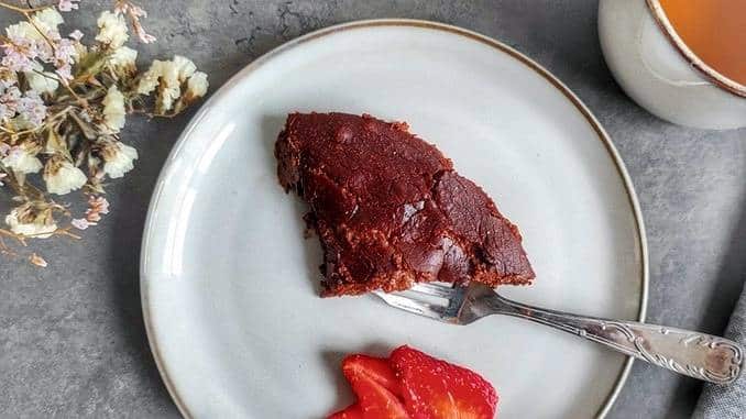 Une part de fondant au chocolat sur une assiette, avec des tranches de fraises sur le côté.