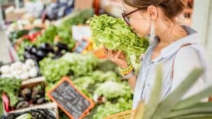 Fruits et légumes stand marché avec une femme qui fait ses achats et sent une laitue