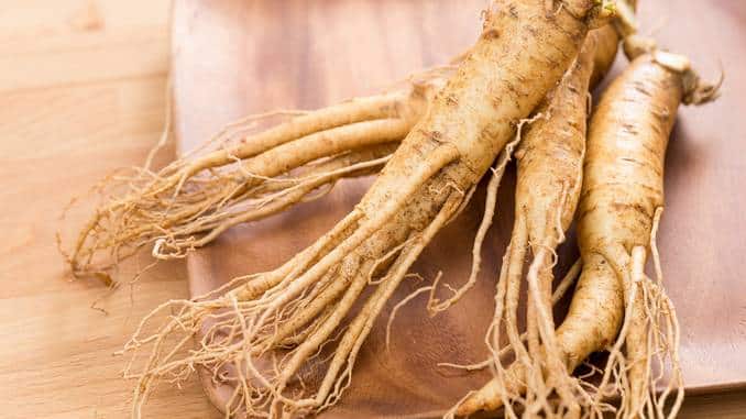 Trois racines de ginseng sur un plateau en bois.