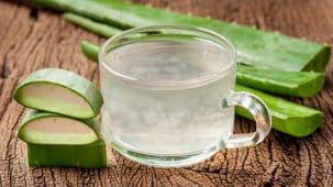 Jus d'aloe vera : boisson dans un verre posé sur du bois. Gros plan sur le verre et l'aloe vera.