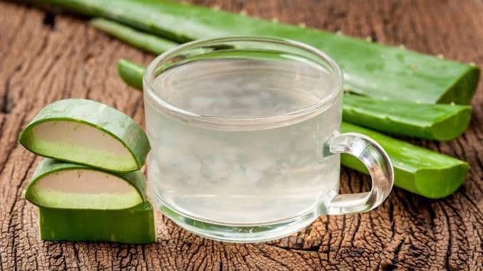 Jus d'aloe vera : boisson dans un verre posé sur du bois. Gros plan sur le verre et l'aloe vera.