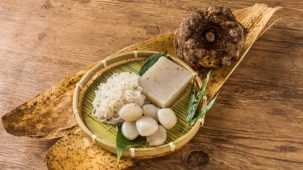 Konjac sous différentes formes : nouilles, feuilles, konnyaku, racine... Une assiette en bois accueille les nouilles, les feuilles et le konnyaku. L'ensemble est posé sur du bois.