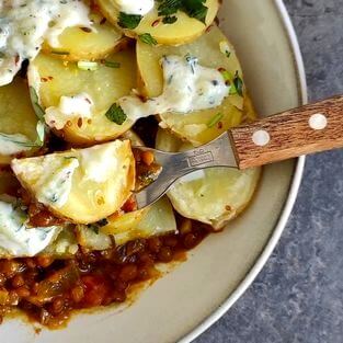 Plat à base de pommes de terre et lentilles au curry. Une sauce au yaourt et aux herbes recouvre le plat.