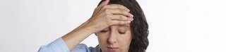 Femme brune qui met sa main sur son front, les yeux baissés. Elle semble avoir mal à la tête, une migraine ou un mal-être passager.