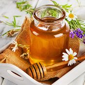 Amla et miel : un pot de miel à côté d'une cuillère à miel en bois. Il y a plusieurs fleurs blanches et bleues autour du pot.