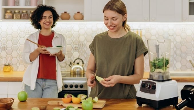 Deux jeunes femmes préparent un jus vert dans leur cuisine pour nettoyer le foie naturellement.