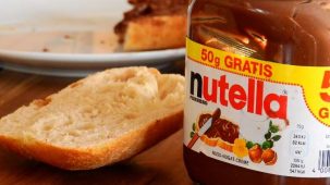 Pot de nutella posé sur une table avec une tartine de pain et une assiette en arrière plan.