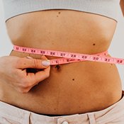 Probiotiques et ventre plat : ventre d'une femme mince qui mesure son tour de taille avec un ruban rose