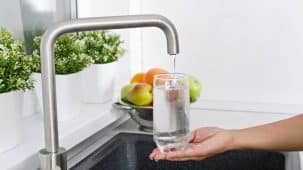 Purificateur d'eau integré sous évier. On aperçoit un verre d'eau rempli d'une eau pure et fraiche dans une cuisine, sous un robinet.