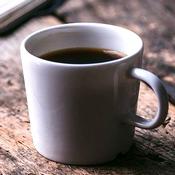 Insomnie et café : une tasse blanche remplie de café sur une table en bois. Le café est un stimulant qui empêche souvent de dormir.