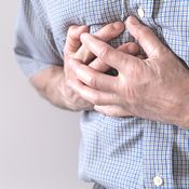 Gros plan sur la poitrine d'un homme en chemise bleue. Il pose sa main sur son cœur et semble avoir un problème cardiovasculaire car sa main est crispée.