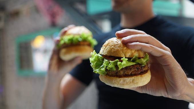 Homme tenant deux hamburgers végétariens dont un est en gros plan dans sa main