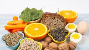 Aliments riches en vitamine B1. On aperçoit des oléagineux, des graines, des oeufs, une demi-orange et des feuilles d'épinards sur une table