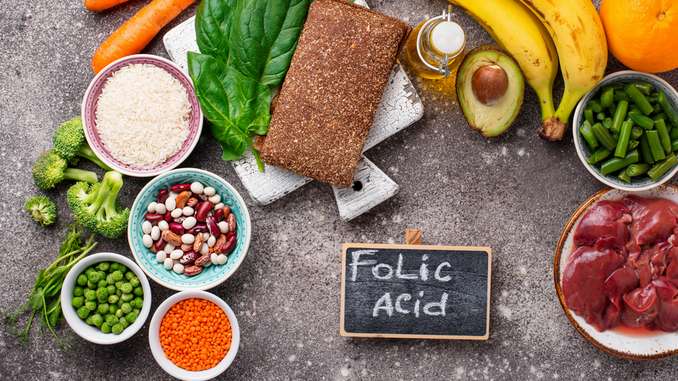 Aliments riches en vitamine B9 disposés sur une table en béton : avocats, graines, lentille, huiles, foie, bananes, épinards, etc.